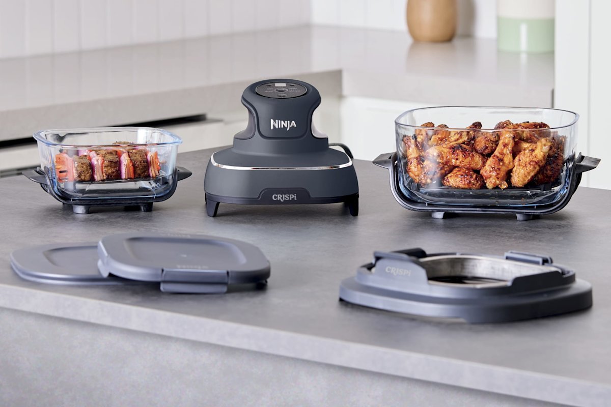 Ninja Crispi PowerPod heating unit set on a countertop between its two glass containers, with storage lids and container adapter